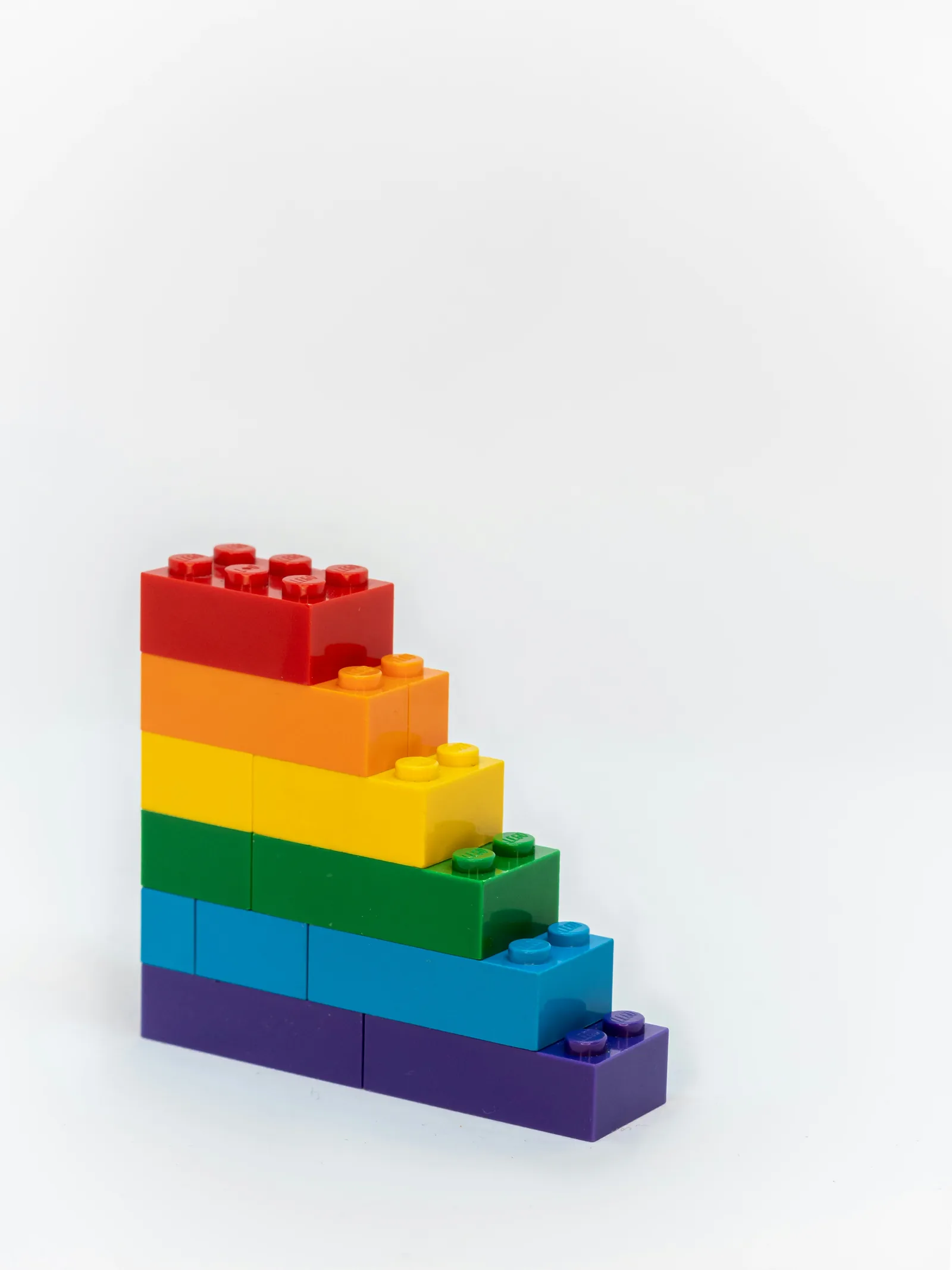 Empilement de briques Lego aux couleurs de l'arc-en-ciel sur fond blanc, formant un escalier coloré et vibrant.