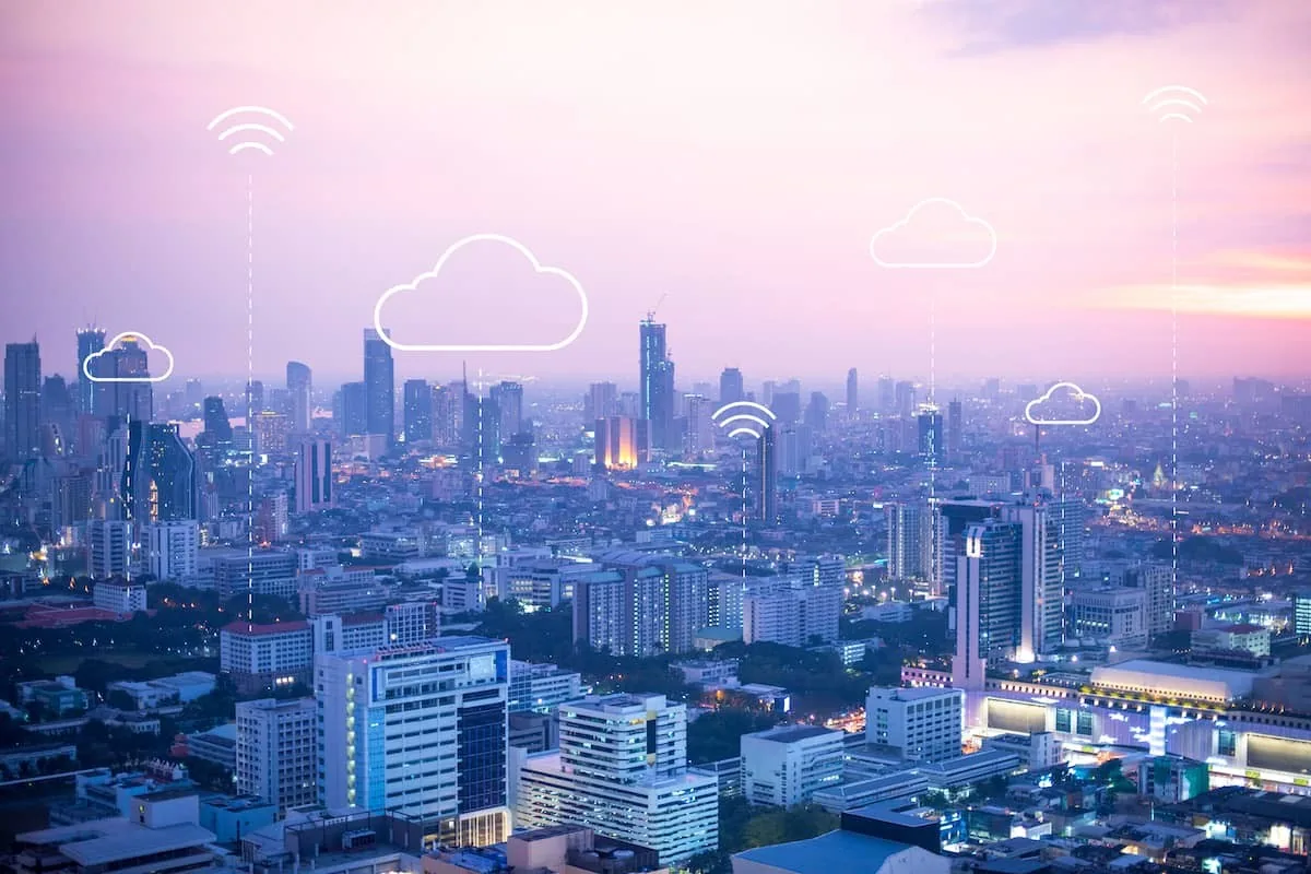 Vue d'une ville au crépuscule sous ciel rose, avec dessins de nuages et symboles Wi-Fi. Gratte-ciel illuminés, ambiance futuriste.
