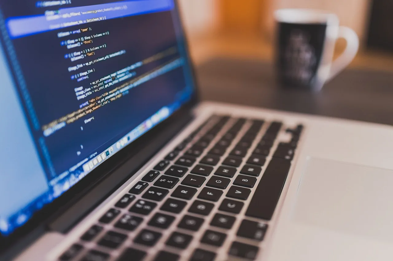 Clavier d'ordinateur avec écran affichant du code sur fond flou. Tasse en arrière-plan. Ambiance studieuse et calme.